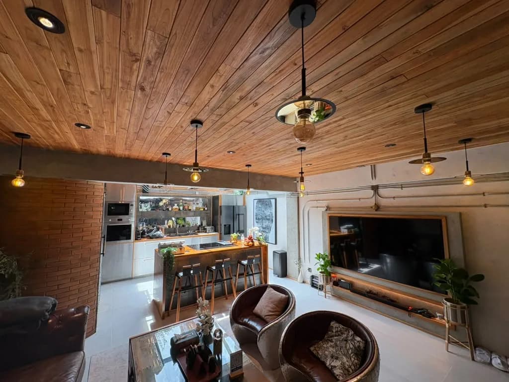 Open-plan living room and kitchen beneath a teak ceiling with pendant lights